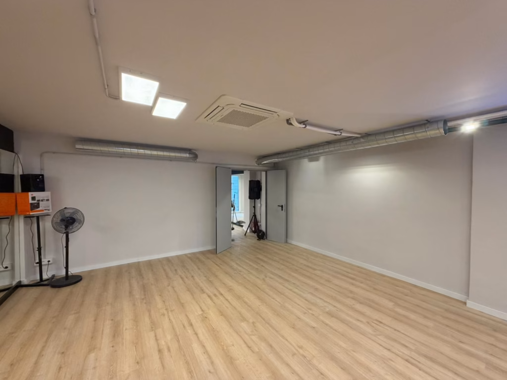Sala de la escuela de baile con suelo de madera y conductos de extracción instalados junto al techo.