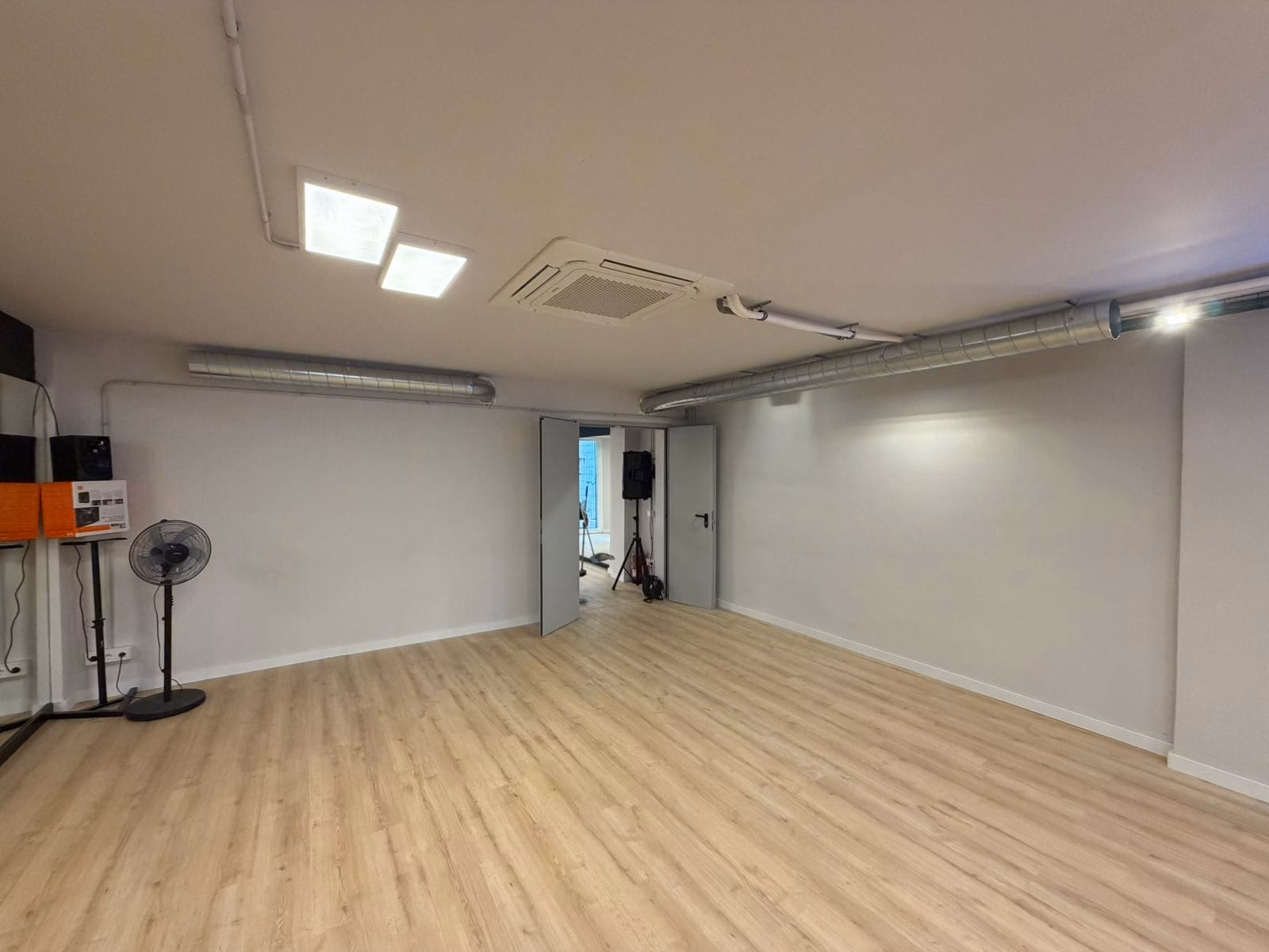 Sala de la escuela de baile con suelo de madera y conductos de extracción instalados junto al techo.