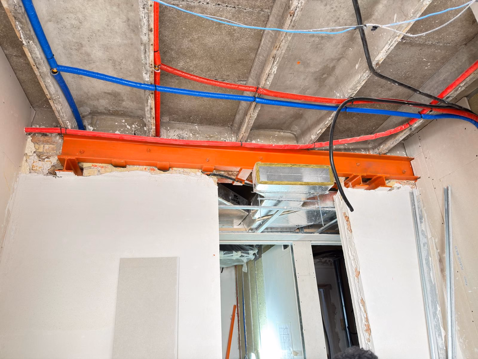 Viga metálica próxima a conductos de climatización, tuberías y cableado en obra.